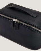 Close-up of a black layflat vanity bag made from full grain leather with a zip-around closure.