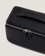 Close-up of a layflat vanity bag in black leather with zip-around closure and handle.