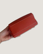 Hand holding a red full grain leather mini pouch showcasing its compact design and structured silhouette.