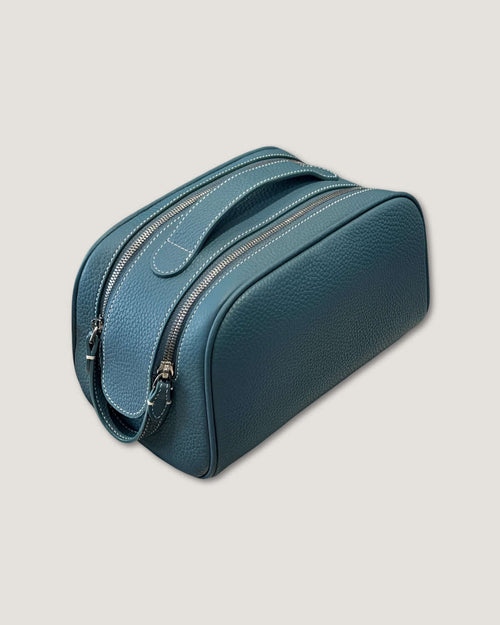 Stylish leather makeup bag in teal color with double zippers and a sturdy handle for easy carrying.