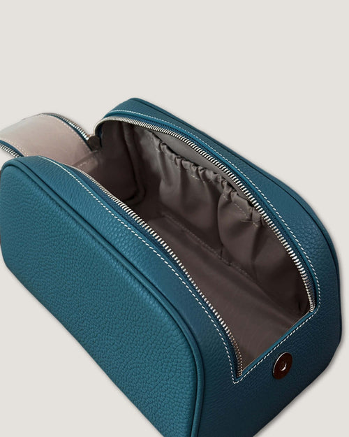 Open view of a leather makeup bag in teal, showcasing its spacious interior and double-zipper design.