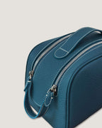 Close-up of a stylish leather makeup bag in teal color, featuring dual zippers and a sturdy handle for easy access.