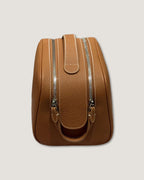 Leather makeup bag with double-zipper design and sturdy handle in a light tan color.