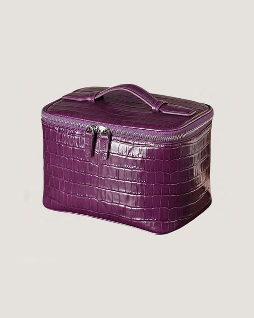 Medium leather train case in purple crocodile texture with zip-around closure and flat top handle.