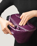 Medium leather train case in purple being held with both hands, showcasing its sleek design and zip-around closure.
