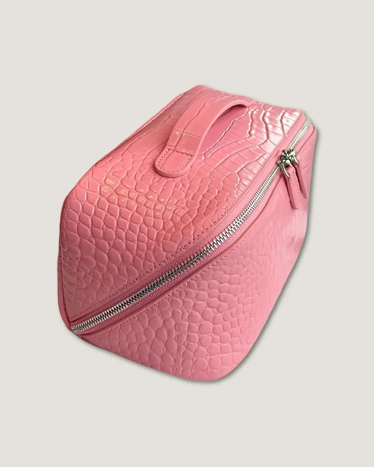 Layflat leather vanity bag in pink featuring a textured finish and zip-around closure.