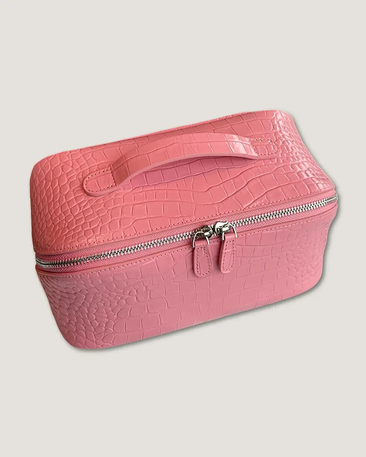 Layflat leather vanity bag in pink crocodile texture with zip-around closure and handle for easy carrying.