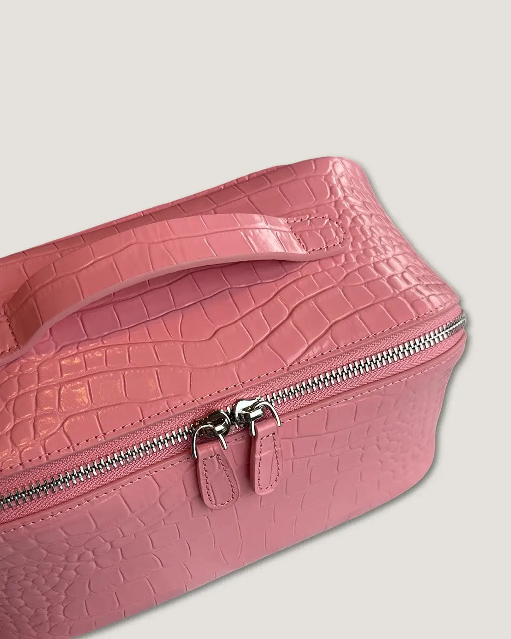 Close-up view of a pink layflat leather vanity bag with croc texture and silver zippers.