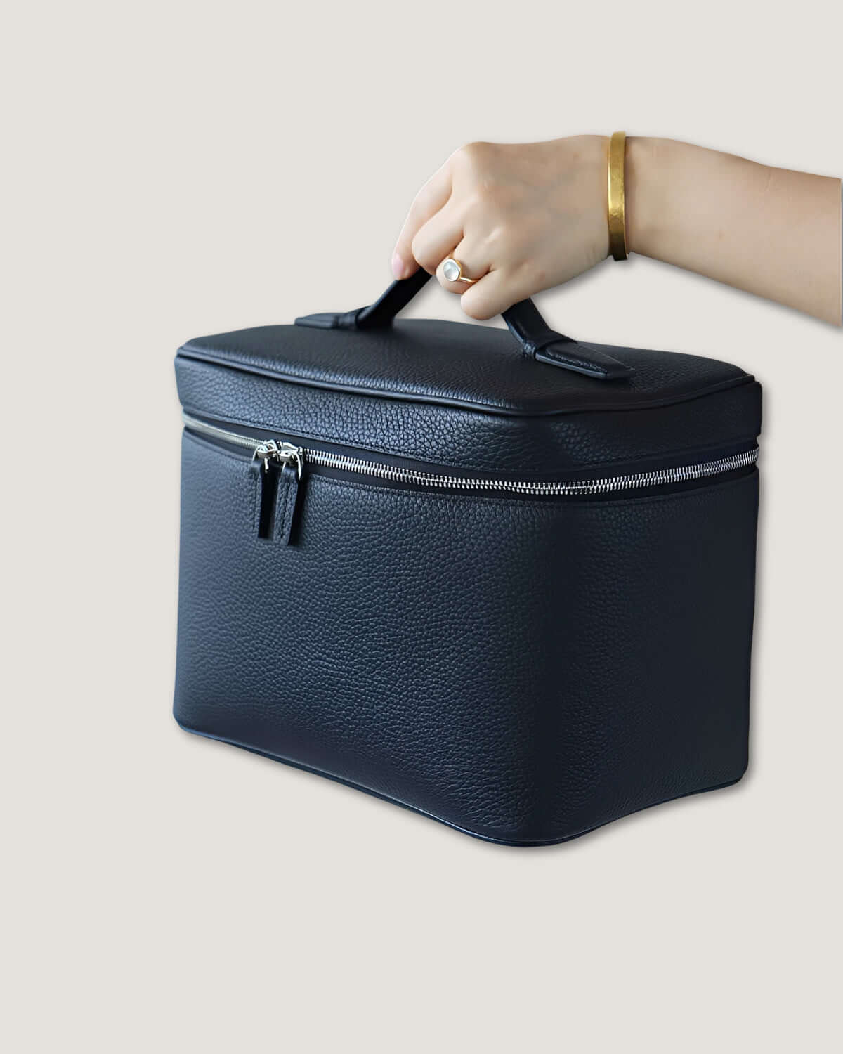 Hand holding a medium leather vanity bag, showcasing its sleek design and zippered closure.