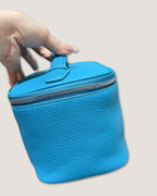 Top view of a medium leather vanity bag in bright blue being held, featuring a zip closure and textured surface.