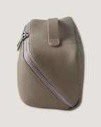 Side view of a layflat vanity bag made of full grain leather with a silver zip-around closure.