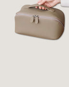 Hand holding a layflat vanity bag made of full grain leather, featuring a zip-around closure and compact design.